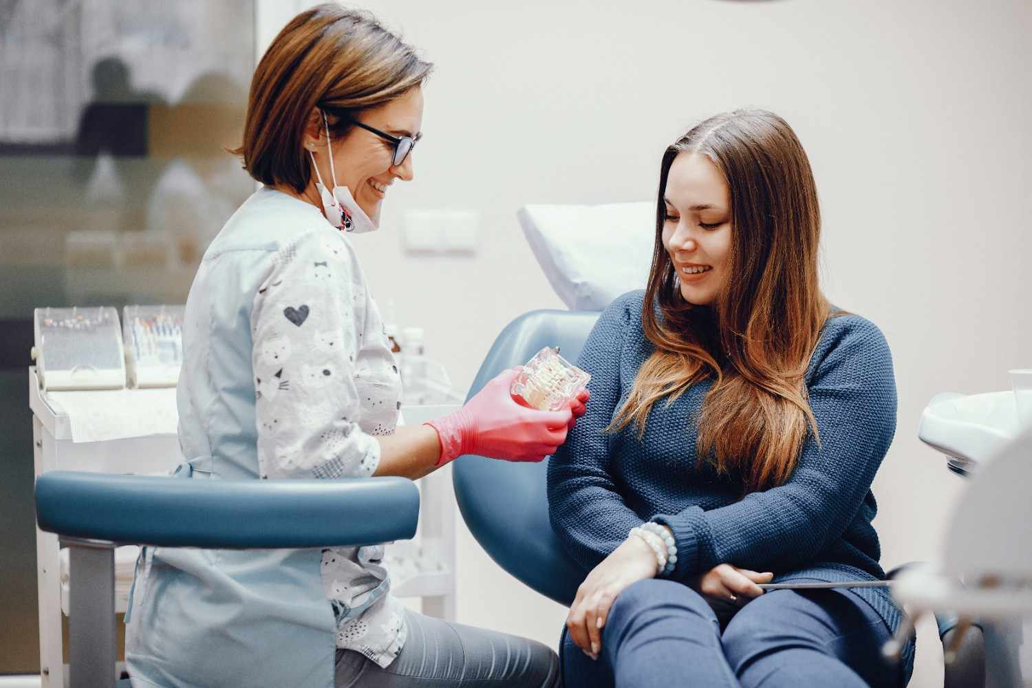 Dentist explaining dental care using a tooth model while an adult patient listens during a consultation in a dental office.