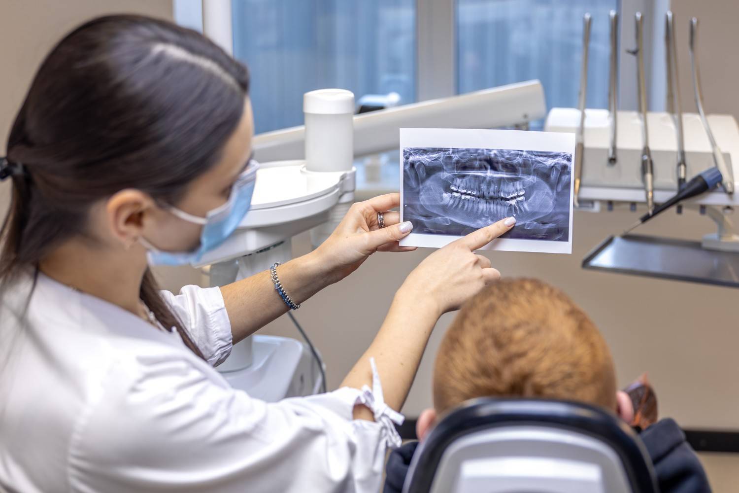 Dentist showing a panoramic dental X-ray to a child patient while seated in a dental chair during an orthodontic consultation.